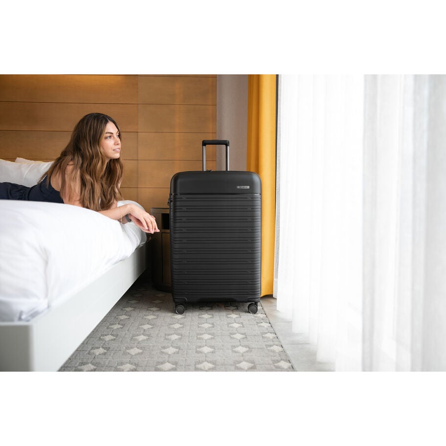 Person with black suitcase near bed in hotel room
